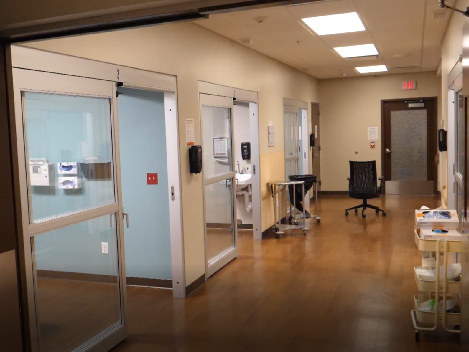 A hallway lined with recovery rooms, with sliding glass doors and privacy blinds.